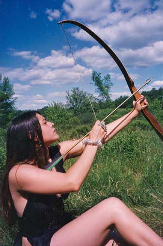 Sexy young, long legged Amazon woman laying in a grassy field with a bow and arrow 