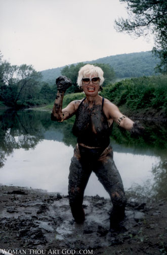 Amazon woman with feet stuck in a pit of mud on the shore of a country island.  Body completely covered in mud with a handful of it ready to sling it at anyone who crosses her