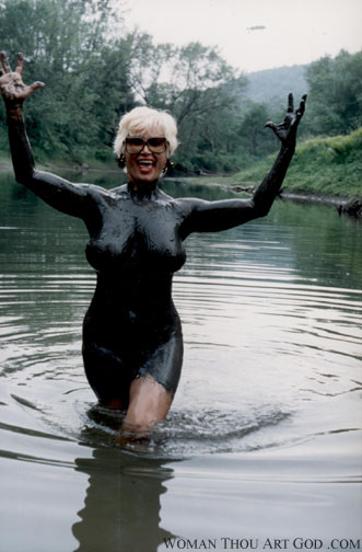 Woman covered in black as oil mud triumphantly immerging out of the water with pangs of fervor